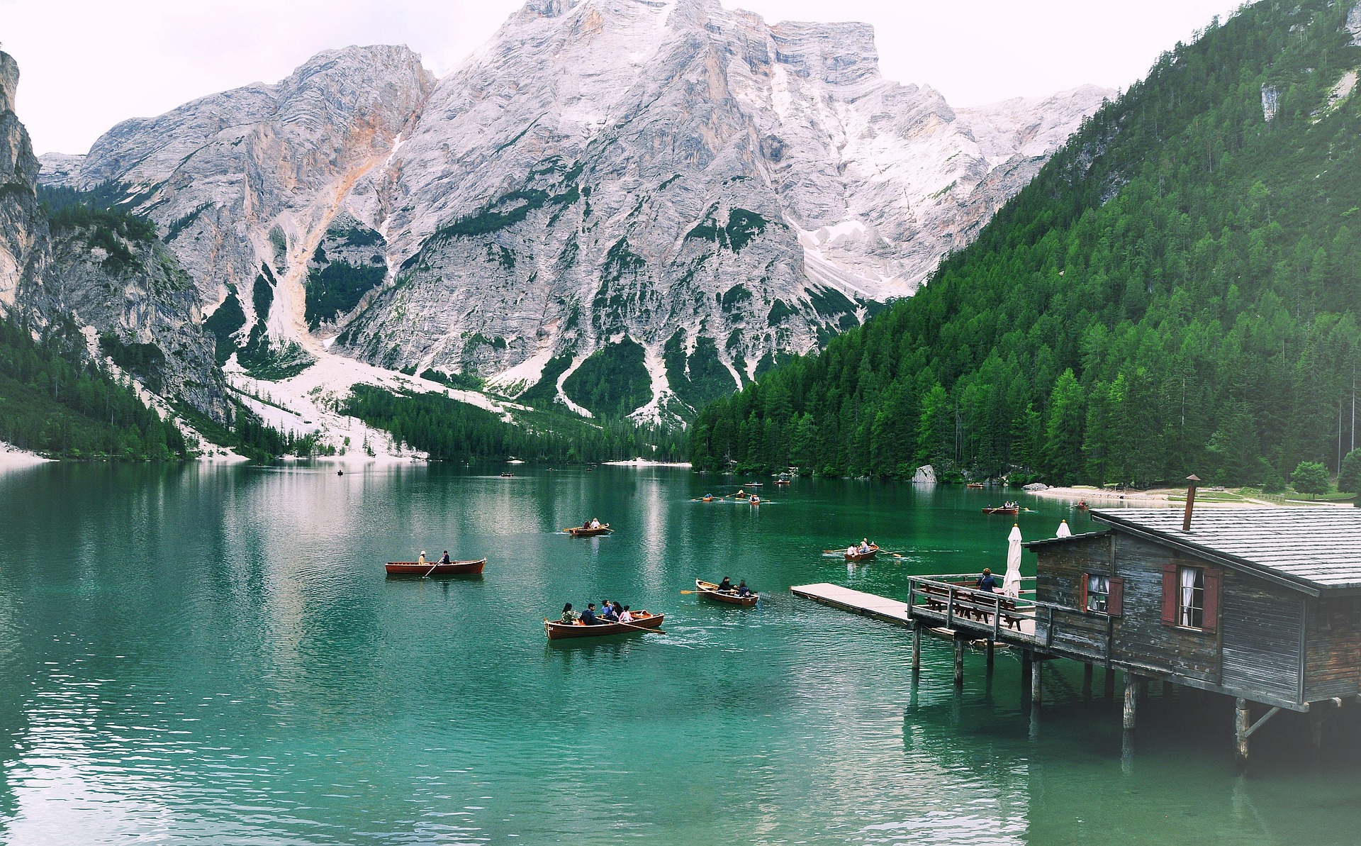 paysage de montagne enneigées avec un lac vert au milieu. des bateaux et un port sont visibles également